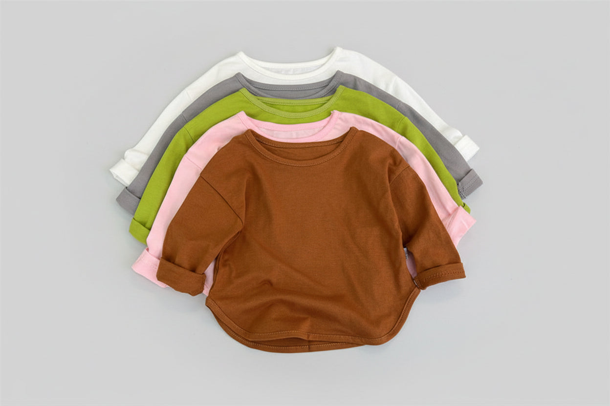 Stack of colorful children's sweatshirts on a wooden floor with slippers and a hat.