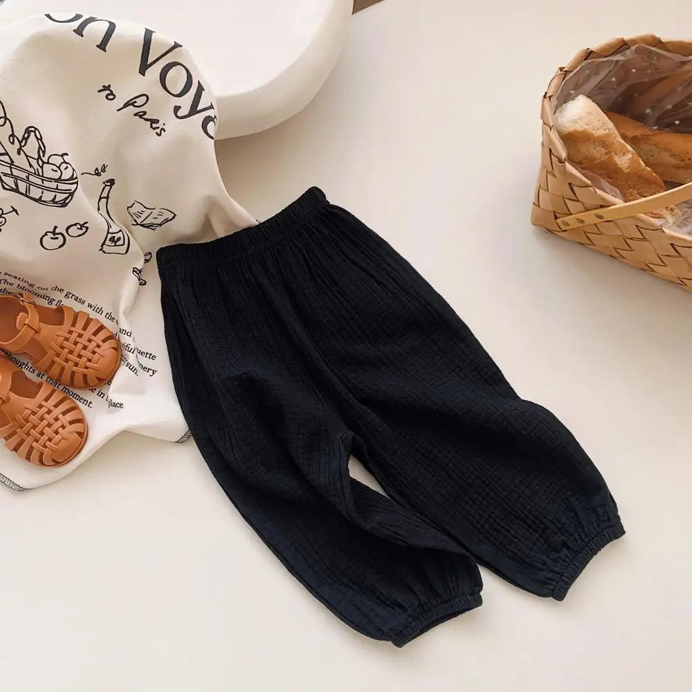 Black baby pants on a light surface with a white shirt featuring shoe illustrations in the background.