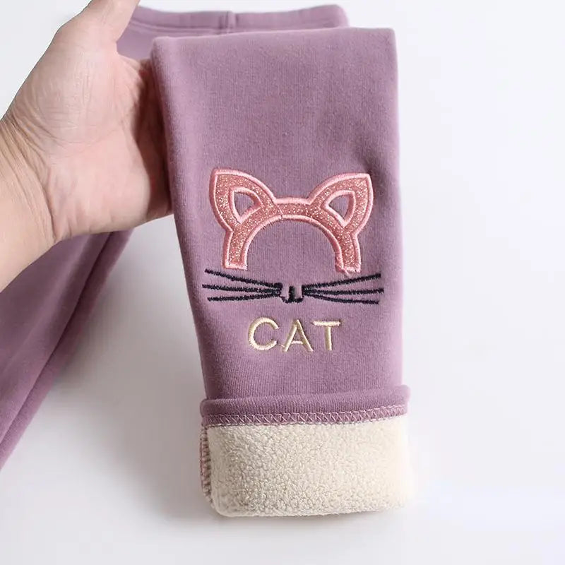 Folded purple leggings with a cat design and 'CAT' text held by a hand on a white background