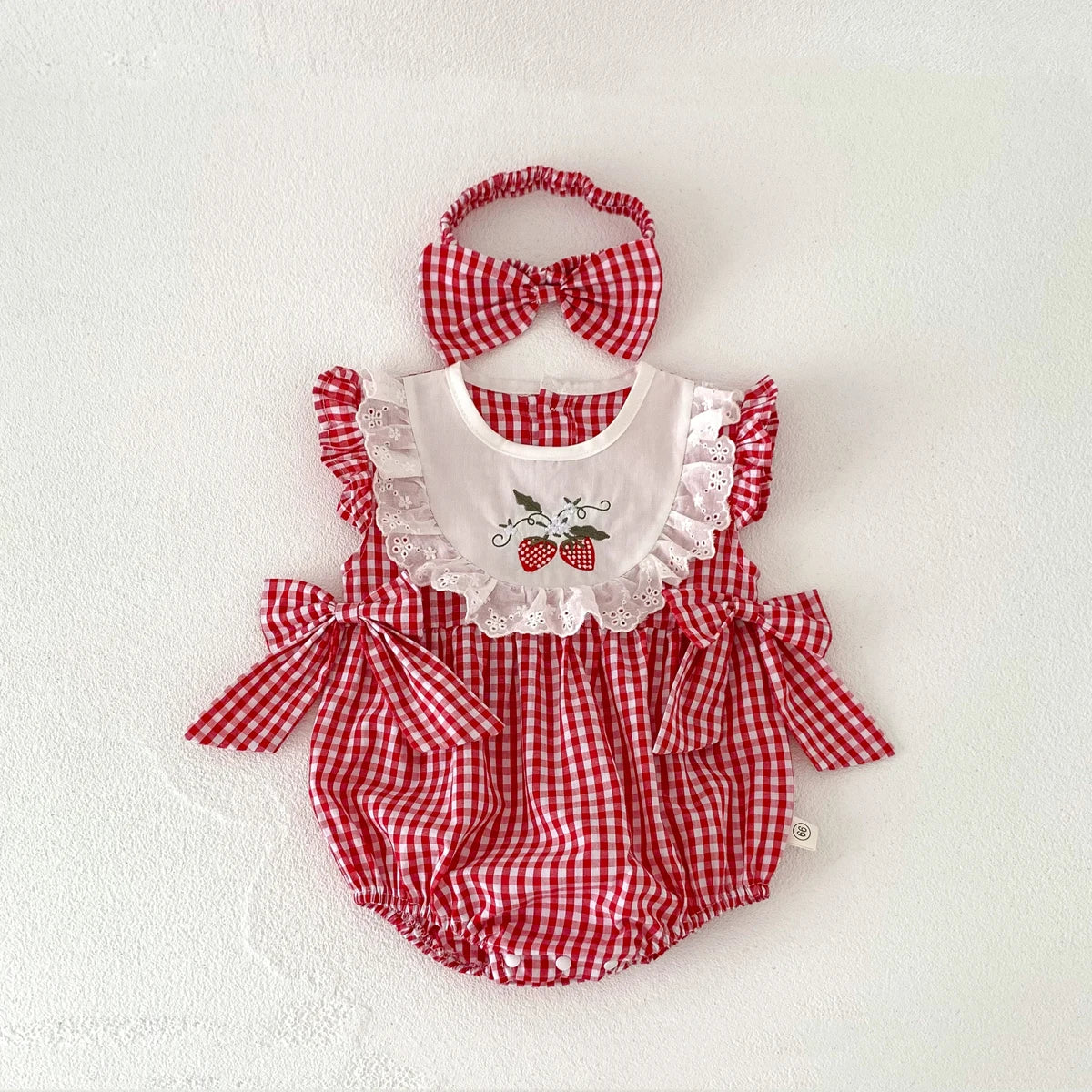 Red and white checkered baby romper with matching headband on a light background
