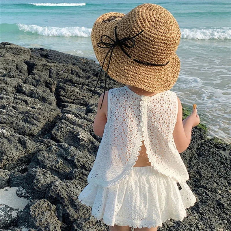 Child wearing a straw hat and white outfit standing on a rocky beach.